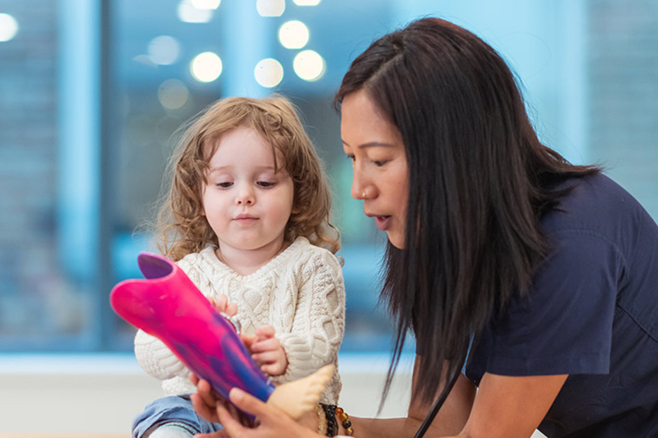 niña pequeña con una enfermera mostrándole una nueva prótesis de pierna